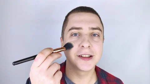 The man looks into the frame and uses powder. Close-up of a guy putting makeup o Stock Footage 146360709