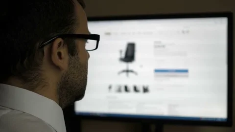 A man looks at the goods in the online furniture store, sitting at the desk. Stock Footage