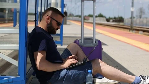 Man looks happy while sitting on the platform and typing something on laptop Stock Footage 78653638