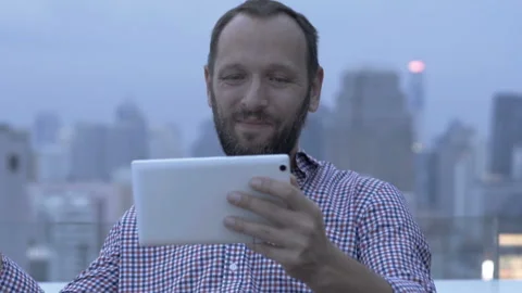 Man looks happy while sitting on the terrace and watching movie on tablet Stock Footage 88103157