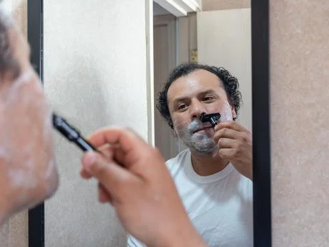 A man looks at himself in the mirror while shaving. Stock Photos