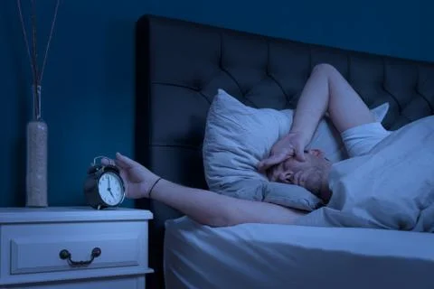 Man looks at his alarm clock at night and cannot sleep Stock Photos