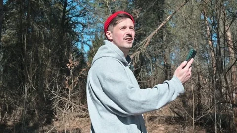 A man looks at his smartphone while standing outdoors in the forest. He's Видео 337642983