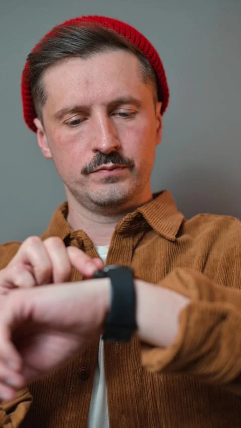 A man looks at his smartwatch while sitting indoors, checking notifications and Stockbeeldmateriaal 337643134