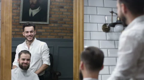 A man looks into a mirror after having his beard groomed at a barber shop. Shot Stock Footage