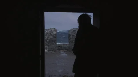Man looks out at ocean waves during rainy evening in a coastal town Stock Footage 325831680