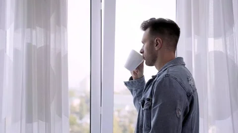 A man looks out the window and drinks delicious coffee from a white Cup Stock-Footage 141562829