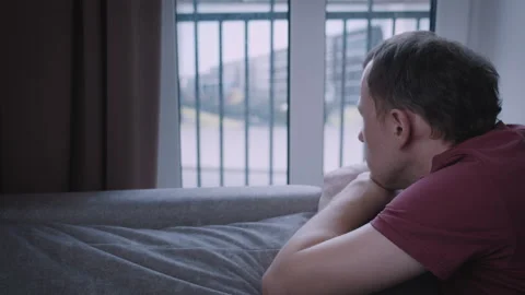 A man looks out of the window, observing the movement outside, leaning on the Stock Footage 315992663