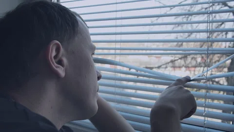 Man looks out the window through the blinds, pushed back with his finger, close Stock Footage 155073516