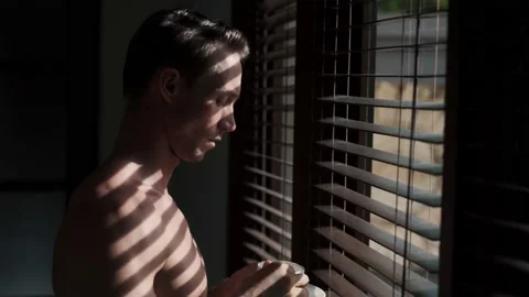 Man looks out window through blinds against the sun, drinks coffee. Stock Footage 160085376