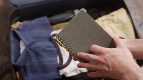 Man looks over a notebook to pack in his suitcase for an adventure Stock-Footage 134286115