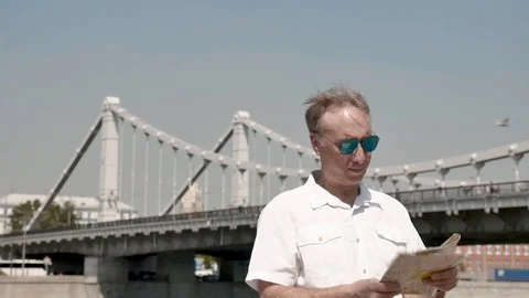 Man looks at a paper map on the background of a large bridge Stock Footage 112422819