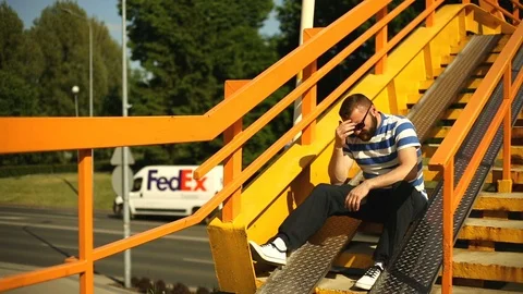 Man looks really worried while sitting on the stairs next to the highway Stock Footage 76979297