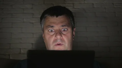 The man looks at the screen of the tablet in a dark room with fright. Head and Stock Footage 92925914