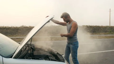 A man looks at a smoking engine of a broken car Stock Footage 79203229