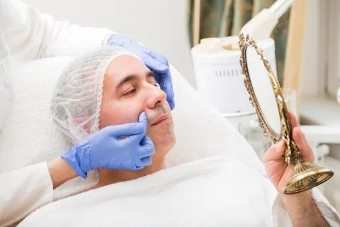 Man looks in table mirror on problem spot on face Foto stock