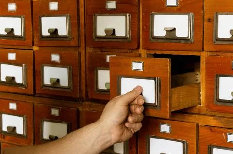 A man looks through the cards in a empty wooden file cabinet with his hand. Stock Photos