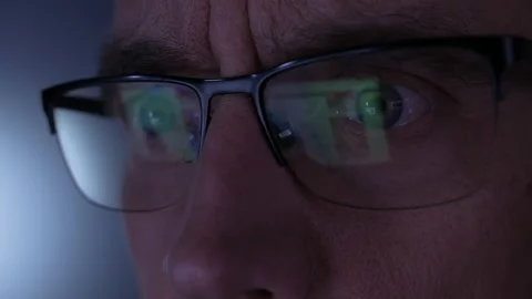 A man looks through glasses, a computer reflecting in the glass while scrolling Vídeo Stock 154165025