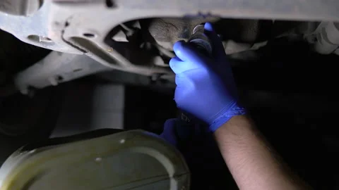 A man loosens a nut under a car engine to drain used oil Stock Footage 134492353