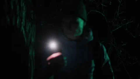 A man lost in a dark forest at night, holding a flashlight and scanning his Stock Footage 304636815
