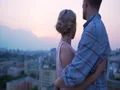 Man in love stroking shoulders of his female lover, admiring sunset on roof 4k or 4k+ Resolution