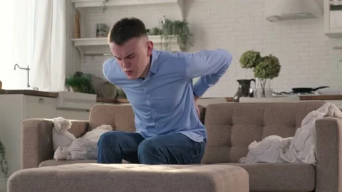 Man with lower back pain sits down on sofa Stock-Footage 170644167