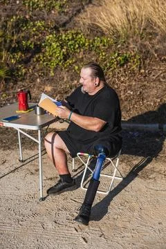Man with lower limb prosthesis reading book outdoors Fotos Stock