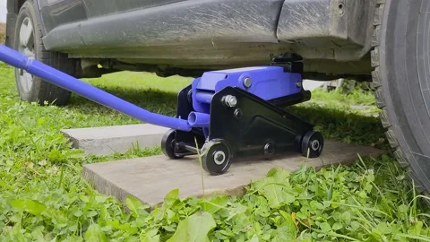 A man lowers a car using a jack after replacing a wheel or tire. Stock Footage 218822160