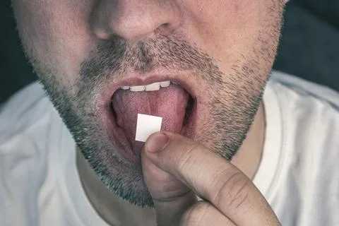 Man with LSD on the tongue. black background. a white stamp with narcotic aci Foto stock
