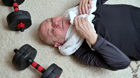 Man Lying After Workout Wiping Sweat With Towel Beside Dumbbells On Carpet Floor Stock Footage 329906334