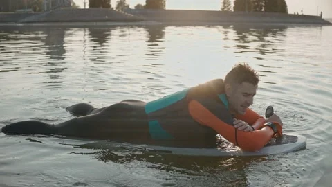 Man lying and smiling on a surfboard wearing wetsuit at warm golden sunset Vídeo Stock 166546505