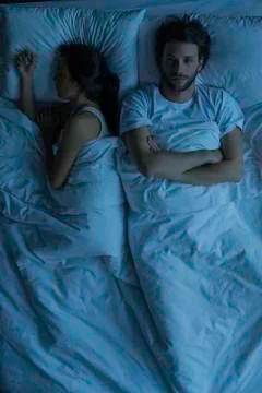 Man lying awake in bed next to sleeping wife Stock Photos