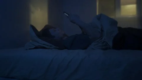 Man lying awake at night, mobile phone screen keeping him awake, blue light Stock Footage 320175650
