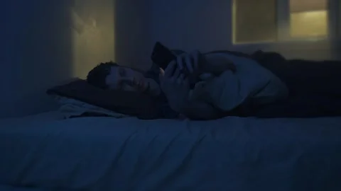 Man lying awake at night, scrolling phone in bed, blue light from screen Stock Footage 320175614