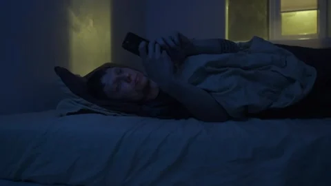 Man lying awake at night scrolling phone in bed, blue screen light causing Stock Footage 320188231