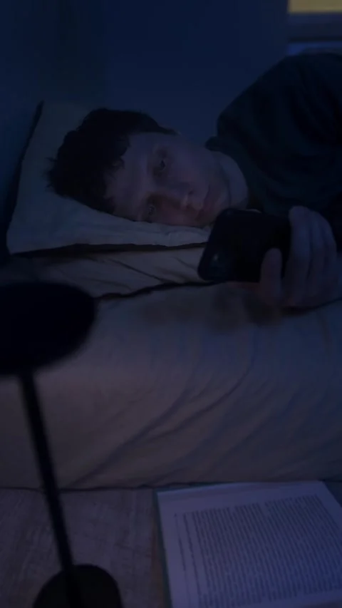 Man lying awake at night scrolling phone in bed, blue screen light causing Stock Footage 320247506