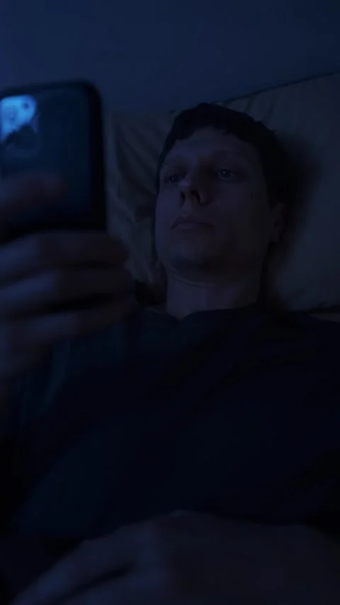 Man lying awake at night scrolling phone in bed, blue screen light causing Stock Footage 320247512