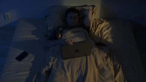 Man lying awake at night using laptop in bed, blue screen light causing insomnia Video stock 320188897