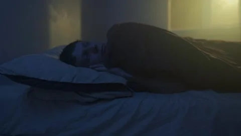 Man lying awake at night, warm yellow window light, insomnia night scene Stock Footage 320175371