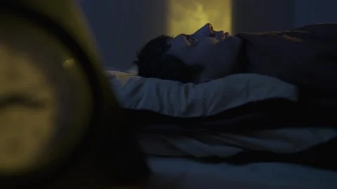 Man lying awake at night, warm yellow window light, insomnia night scene 스톡 동영상 320188044
