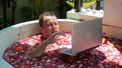Man lying in the bath and chatting on laptop Stock Footage 40330649