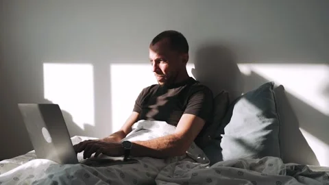 A man is lying on a bed and covered with a blanket working on a laptop A Stock-Footage 154271089