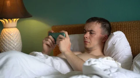 Man is lying in bed and is using the application on his smartphone Stock Footage 75652772
