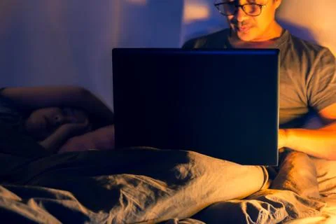 Man lying in bed and working with laptop late at night. Stock Photos