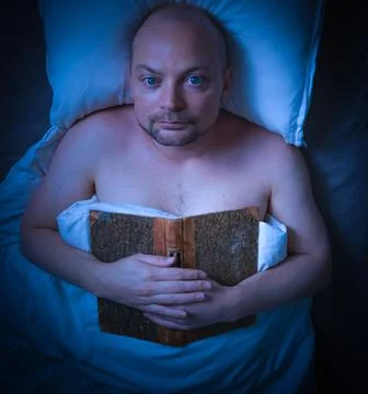 Man lying in bed with a book looking thoughtful. Stock Photos