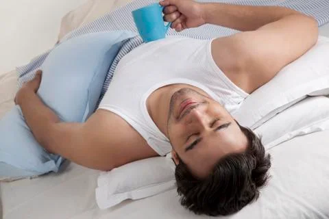 Man lying in bed with a cup of coffee Foto stock