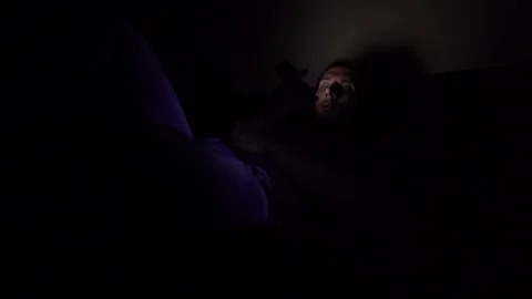 The man is lying on the bed in a dark room and looking at the telephone 库存影片 122139768