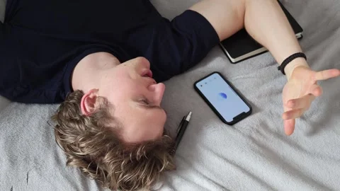 Man lying on bed gazes at smartphone screen symbolizing communication with artif Stock Footage 314979799