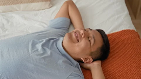 Man lying on bed with hand behind head, eyes closed and slight smile in stu.. Stock Footage 337357891
