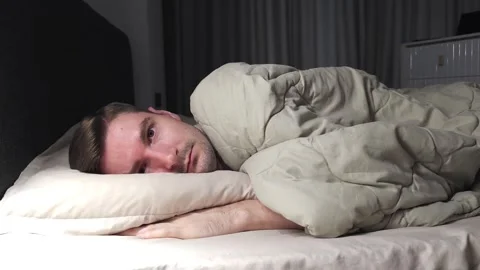 Man lying on a bed with head on pillow wrapped in beige blanket Stock Footage 284042288